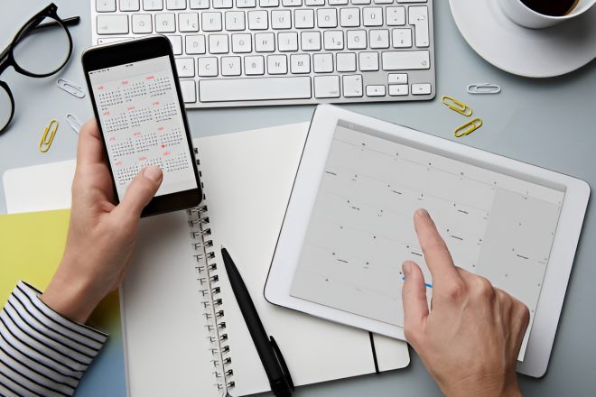 top-view-of-woman-holding-smartphone-and-tablet-with-calendar-on-desk_enhanced (1)